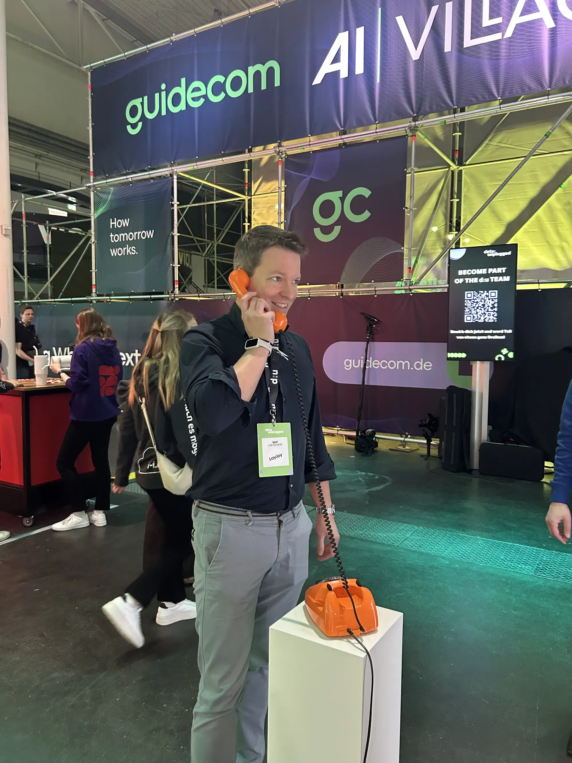 Unser CEO Ulf Loetschert probiert das orangefarbene Telefon aus und redet mit dem Voice Agent