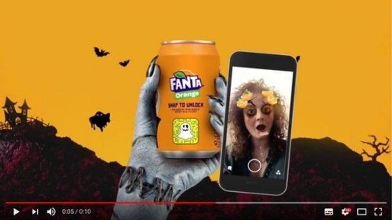 A screenshot from a video is shown. A zombie hand is holding a Fanta can and a woman is using a snapchat Halloween filter.