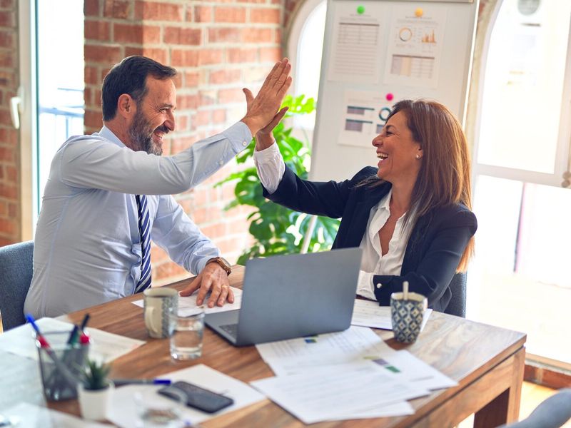 Two people in an office are smiling and exchanging a high-five with each other.