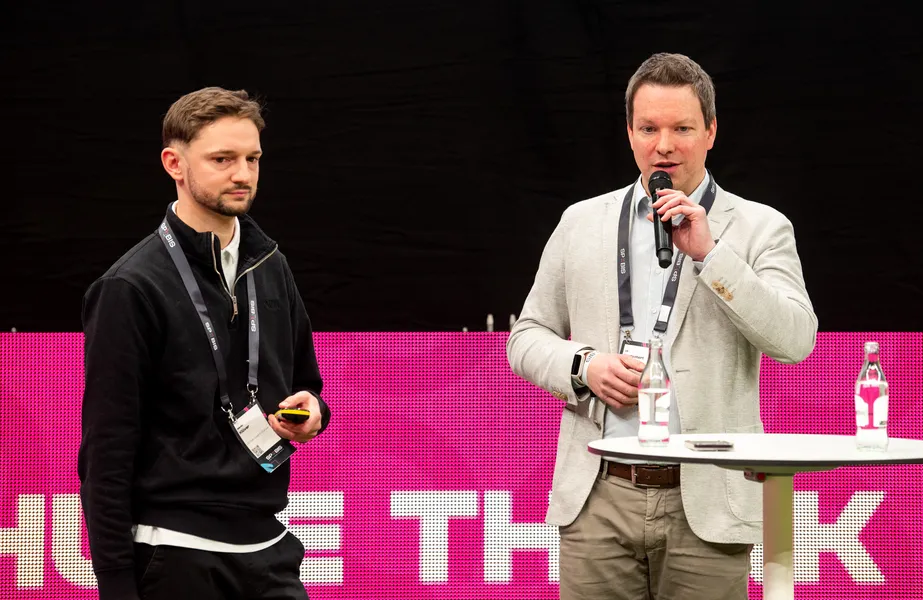 Auf dem Bild stehen unser CEO Ulf Loetschert und Merlin Klüver vom 1. FC Köln gemeinsam auf einer Bühne der SPOBIS 2026 vor einer leuchtend pinkfarbenen Videowand.