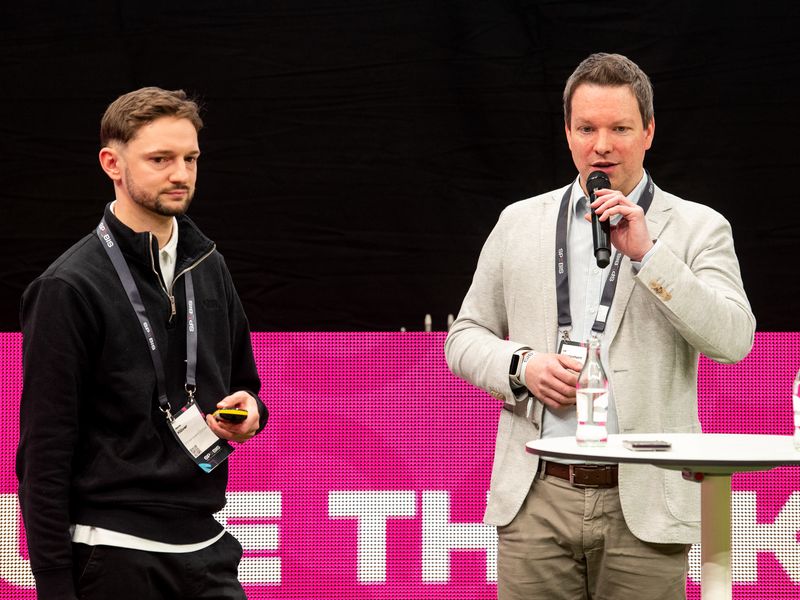 The picture shows our CEO Ulf Loetschert and Merlin Klüver from 1. FC Köln standing together on stage at SPOBIS 2026 in front of a bright pink video wall.