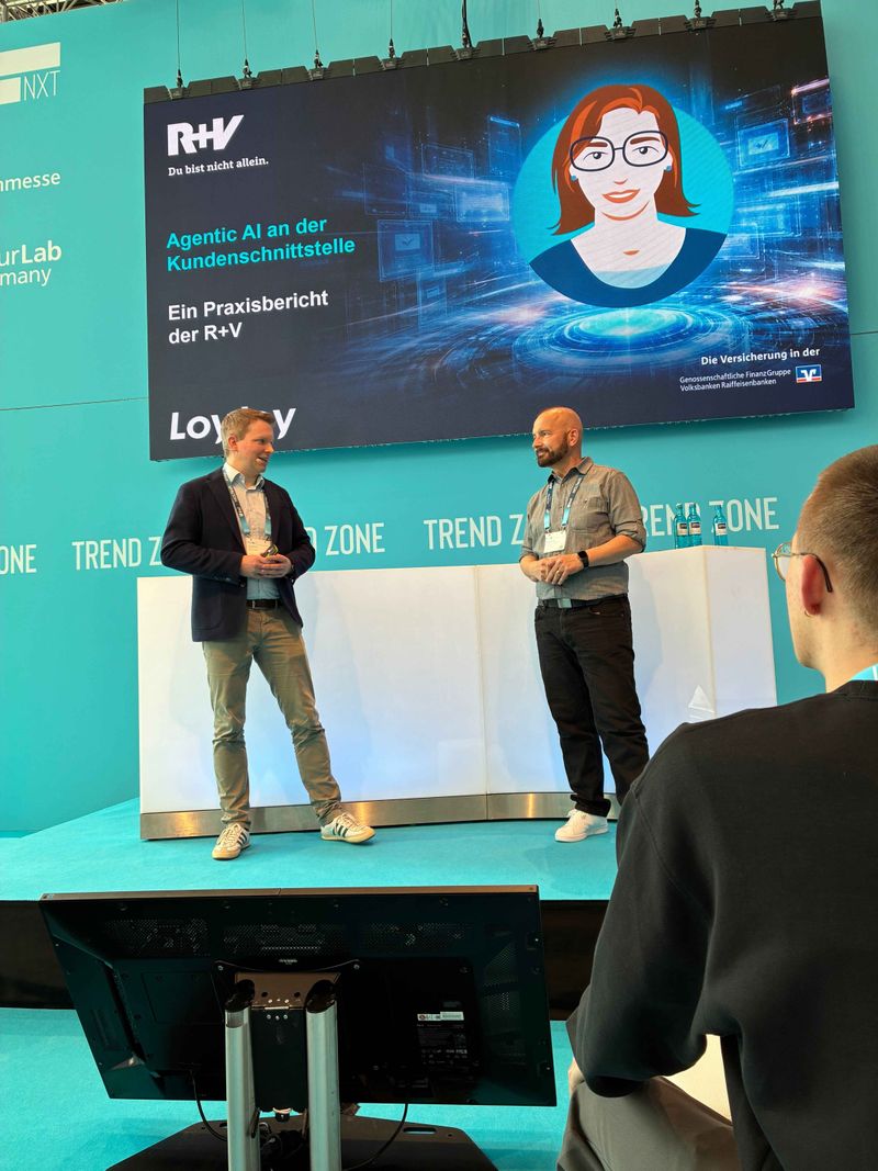 Ulf Loetschert from LoyJoy and Peter Paul Nasim from R+V Versicherung are giving a joint presentation on stage at insureNXT in the Trend Zone. In the background, a large screen displays the presentation entitled ‘Agentic AI at the customer interface’.